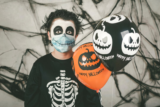 Happy Halloween. kid wearing medical mask in a skeleton costume with halloween balloons