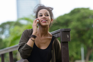 Portrait of happy young beautiful African woman talking on the phone at the park