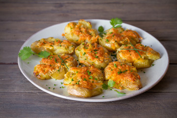 Smashed new baby potatoes with garlic butter and cheese on wooden background close up. Clean eating