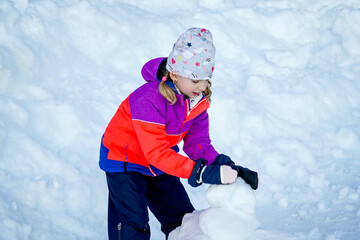 Fototapeta na wymiar Outdoor winter portrait of little cute girl in the sunglasses and wearing ski clothes. Girl playing with snowballs.