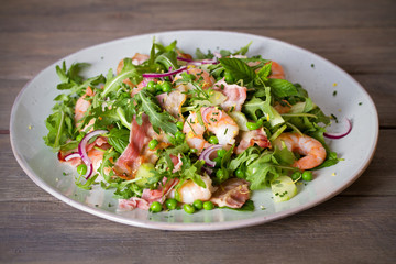 Shrimp salad with bacon, cucumber and radish on wooden background close up. Clean eating