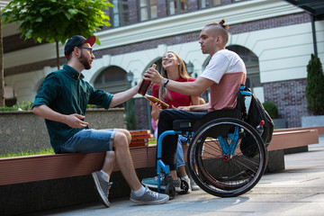 Group of friends taking a stroll on city's street in summer day. Disabled, handicapped man with his friends having fun. Inclusion and diversity concept, normal lifestyle of special groups of society.