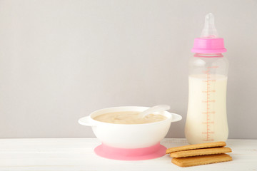 Milk and bowl with porridge for baby on grey background