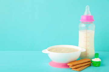 Milk and bowl with porridge for baby on blue background