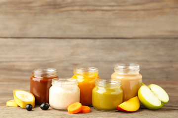 Glass jars with nutrient baby food and fruit on grey background
