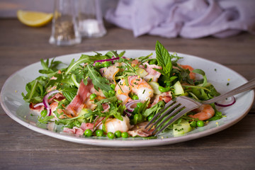 Shrimp salad with bacon, cucumber and radish on wooden background close up. Clean eating