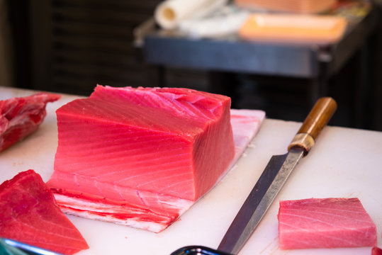 Fresh and raw big tuna fish was cut into pieces at the Tsukiji fish market, Japan..Fresh tuna & salmon fish with chef knife, Japanese food..Akami Tuna Sashimi for sell at the restaurant.