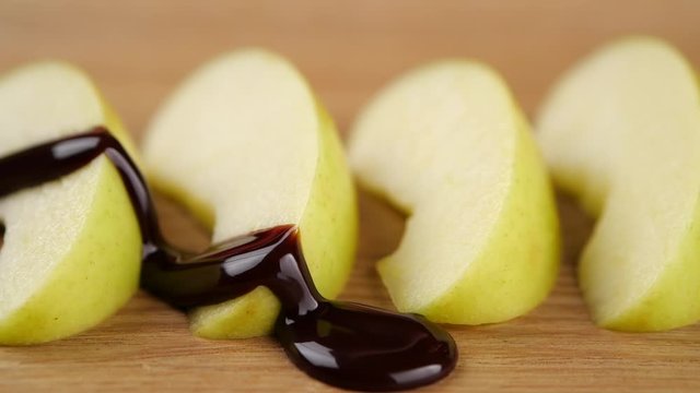 Closeup trickle of chocolate sauce spilling on slices of fresh ripe apple during dessert preparation