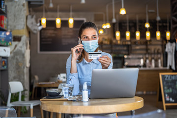 Portrait of young business woman wearing mask while doing shopping online and payment by credit cards. Conceptual of new normal lifestyle during covid-19 pandemic.