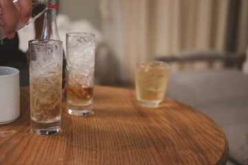 Glass of whiskey with ice on a wooden table in room at hotel.