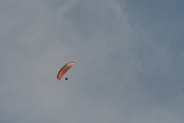 Ein Mann segelt durch die Luft mit seinem hell orangenen Segel. Der Himmel hat sehr dünne Schleier Wolken.