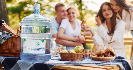 Big plastic water bottle on table. Group of young people have vacation outdoors in the forest. Conception of weekend and friendship