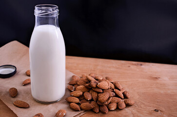 Homemade almond milk in glass bootle with scattered almond on the wooden table. Organic alternative milk. Copy space. Vegan milk from almonds nuts.