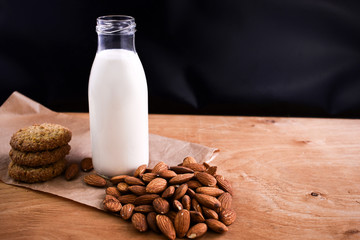 Homemade almond milk in glass bootle with oatmeal cookies and almond on the wooden table. Organic alternative milk. Copy space. Vegan milk from almonds nuts.