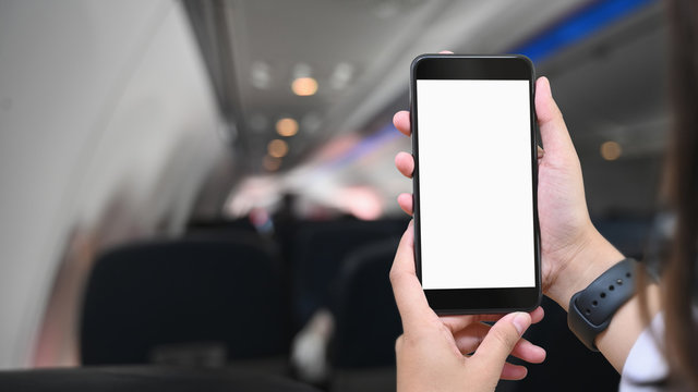 Cropped image of hands is using a white blank screen smartphone in the plane.
