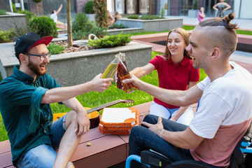 Beer time. Group of friends taking a stroll on city's street in summer day. Handicapped man with...