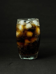 A cool glass of cola drink with ice, bubbles and fizz. Cola in glass with ice cubes isolated on dark background.