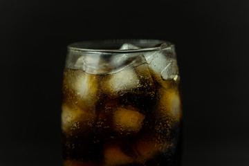 A cool glass of cola drink with ice, bubbles and fizz. Cola in glass with ice cubes isolated on dark background.