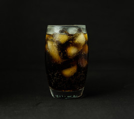 A cool glass of cola drink with ice, bubbles and fizz. Cola in glass with ice cubes isolated on dark background.