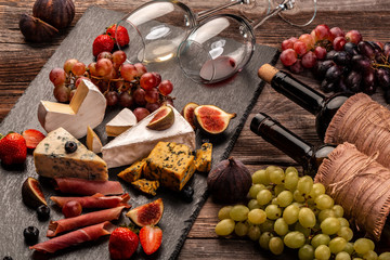 still life, food composition with assorted cheese, glass of wine and fruits on a wooden table