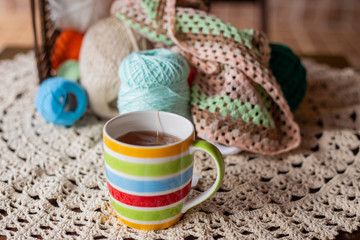 Caneca colorida com chá quente, sobre a mesa com novelos e crochê ao fundo.