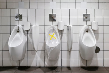 prohibition tape with plastic wrap over urinal in public toilet for people to follow social...