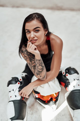 Fototapeta na wymiar Brunette girl with tattoos in a black and red tracksuit, white boots and with a motorcycle helmet, posing in a white photo studio, sitting on the floor