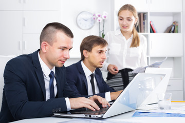 Fototapeta premium Serious active man manager sitting with colleagues and working on laptop in office