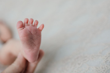 A mom holding newborn baby boy girl feet on a light-colored white blanket with copy space