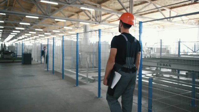 Employee in grey uniform and with orange hard hat walks in the factory.