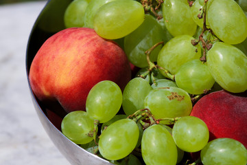 Detail of aluminum container with grapes and peaches on marble table. View from above.