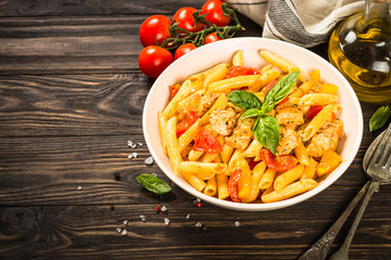 Pasta with chicken and vegetables at wooden table.