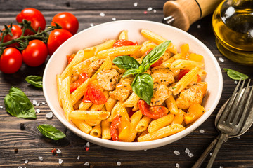 Pasta with chicken and vegetables at wooden table.