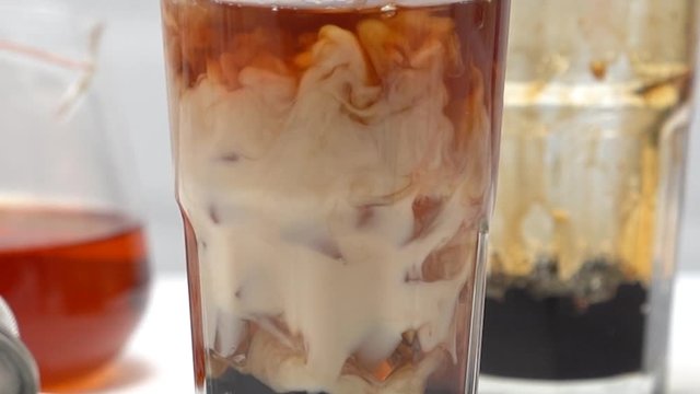 Making bubble tea, pouring blend milk and tea into brown sugar pattern drinking glass cup on white wooden table background, close up, macro, HD studio shot.