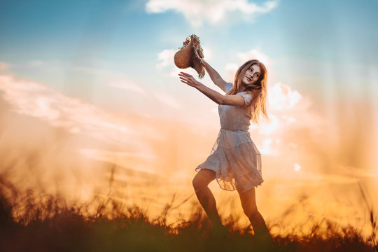 Ginger girl running through the field, holding a summer hat. Copy space