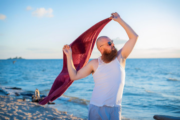 Brutal man posing on the beach with a pareo. A parody of a glamorous girl.