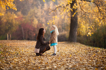 Mom sitting down and talking to her little daughter at eye level, holding her hands in the autumn...
