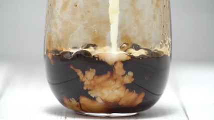 Making bubble tea, pouring blend milk and tea into brown sugar pattern drinking glass cup on white wooden table background, close up, macro, HD studio shot.