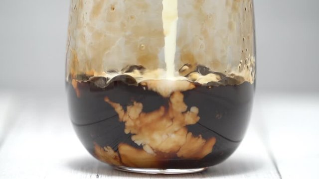Making bubble tea, pouring blend milk and tea into brown sugar pattern drinking glass cup on white wooden table background, close up, macro, HD studio shot.