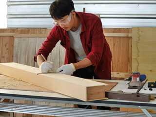 young man Asian carpenter with red shirt  in workshop store working on wood plank and measurement...
