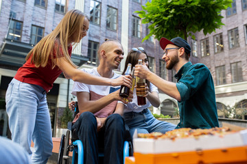 Bottles clinking. Group of friends taking a stroll on city's street in summer day. Handicapped man...