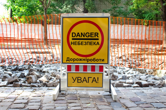 Inner city road with old pavement, closed by stone roadblocks during reconstruction. Yellow roadsign with the words in Ukrainian mean - DANGER, ROAD WORKS, ATTENTION. City street under reconstruction