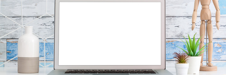 Obraz premium Desk with an open laptop and office supplies. Screen mockup. Wooden puppet. Geometric toolbox. A wall of old wooden boards. Panorama.