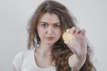 Young woman holds bitcoin coin in her hand, demonstrates financial success. Rising exchange rates of virtual currencies