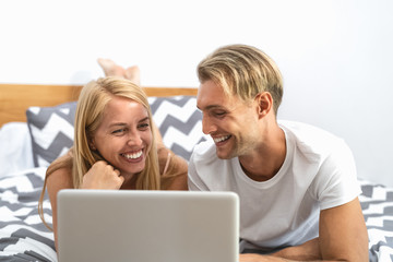 Happy couple lying on bed while using laptop computer - Happy people having funny movie bed time - Love relationship and technology concept