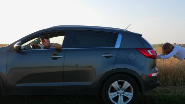young girl pushing a broken car in the field. The man is driving. Bad husband