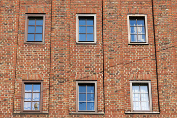 Fototapeta na wymiar A red brick wall with six windows. Some of them are half open, some of them are closed.