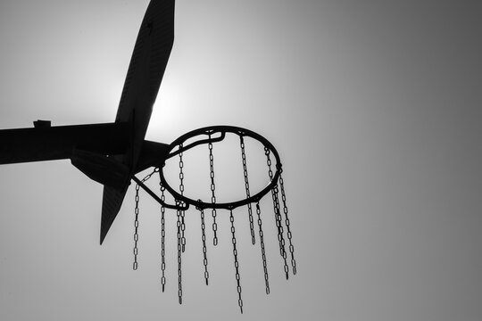 High contrast black and white image of basketball hoop backlit silhouetted with sun flare, black and white