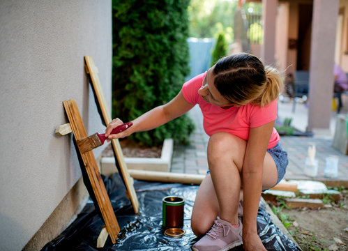 Young Caucasian woman wearing casual clothing painting small wooden fence in her backyard