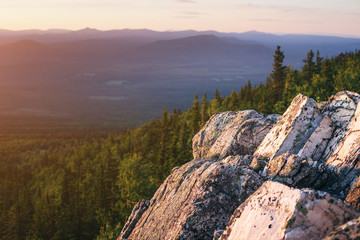 A rocky mountain range covered with forest is illuminated by the pink light of the setting sun. A natural Park or reserve or hunting grounds. Recreational tourism